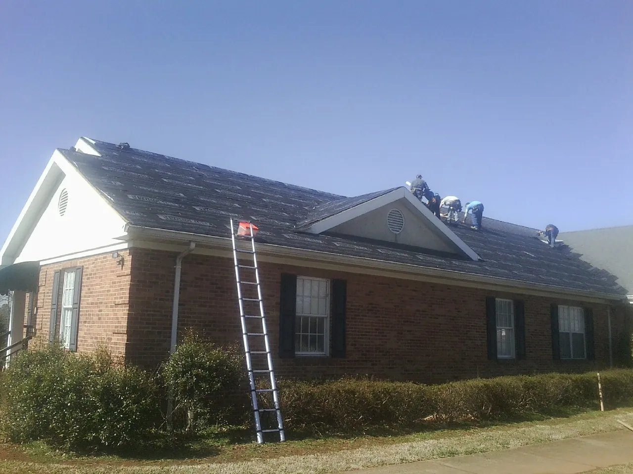 Crew tearing shingles off a brick ranch roof with a ladder set — Metal Roof Repair work by our crew in Tabiona