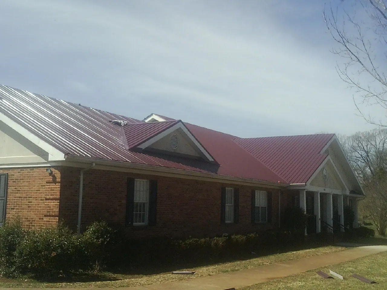Red metal roof with gabled entries on a long brick building, from a Hail Damage Roof Repair job in Tabiona