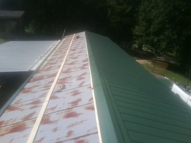 Old rusted panels beside newly installed green metal roofing — Wind Damage Roof Repair by Roofing Brothers in Tabiona