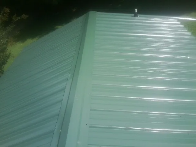 New green metal panels meeting at the ridge of a roof — Flat Roof Repair work by our crew in Tabiona