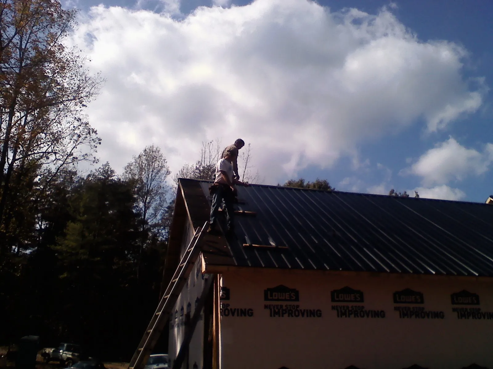 Roofer fastening dark metal panels high against a cloudy sky, from a Roof Inspection job in Tabiona