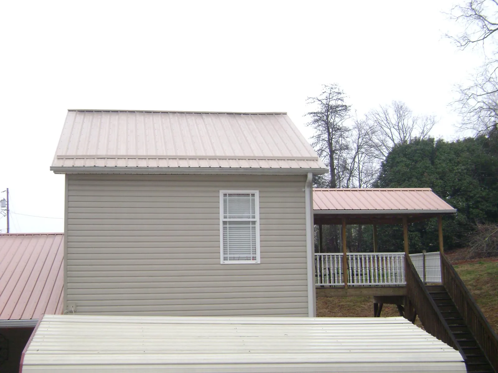 Tan metal roofs on a two story addition and attached porch, from a Roof Replacement job in Tabiona